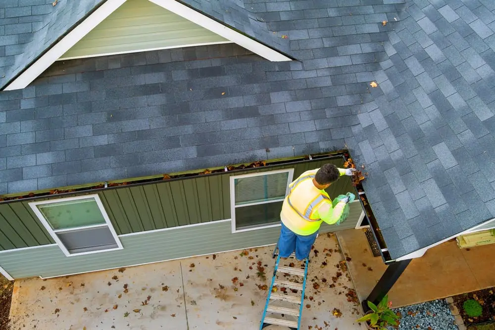 Worker clearing clogs from a roof gutter by hand