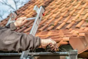 Man on ladder cleaning house gutters