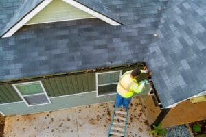 How To Clean Gutters: A Complete Guide 1 Worker clearing clogs from a roof gutter by hand