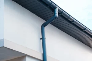 Dark blue round gutter and downspout installed on a white modern house exterior