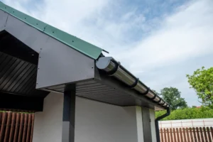 Dark gray round metal rain gutter system installed on a modern house with green metal roof and downspout